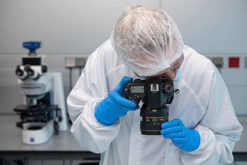 Onderzoeker houdt een fotocamera vast en fotografeert een bewijsstuk op de labtafel.