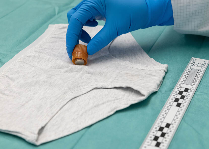 Hand in blauwe handschoen stempelt op een grijze onderbroek om zo biologische sporen te verzamelen.