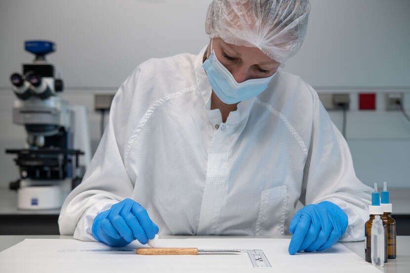 Onderzoeker draagt een haarnetje, handschoenen en een mondkapje en doet onderzoek aan een keukenmesje