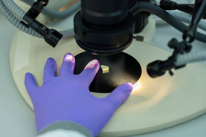 Hand in paarse handschoen naast een pil onder een microscoop.