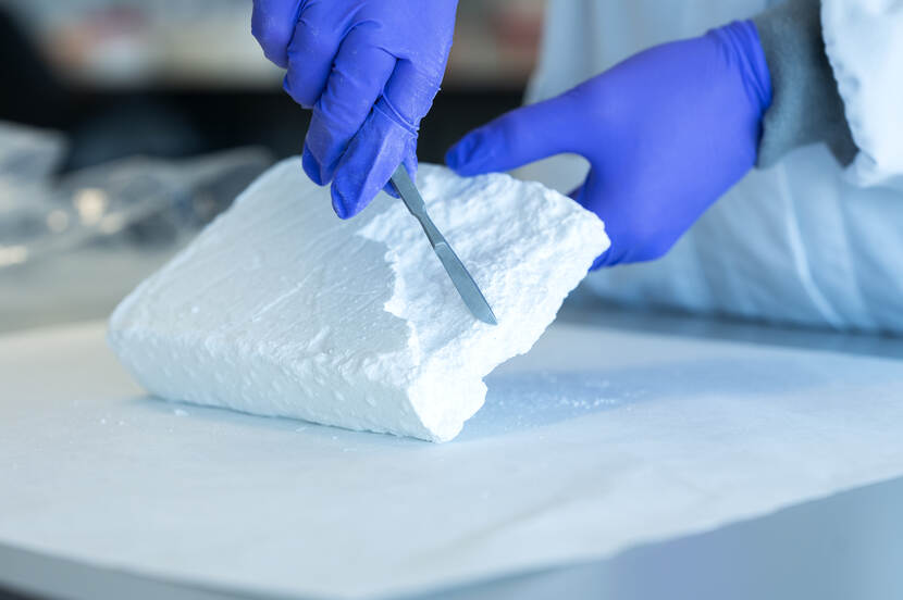 Onderzoeker schraapt met een mesje over een groot blok drugs.